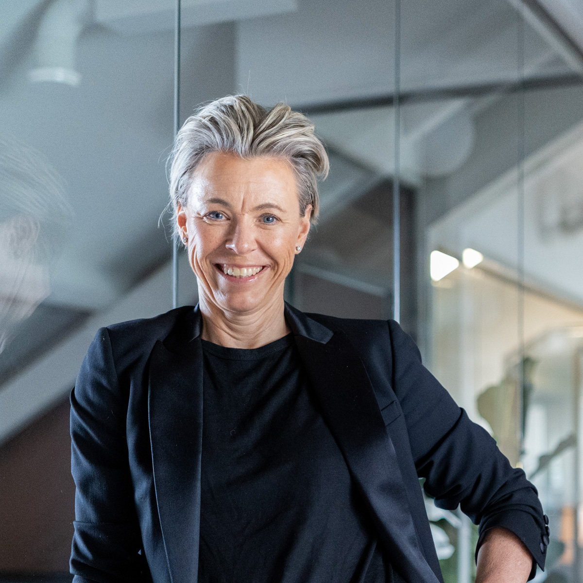 En kvinne med krøllete hår smiler mens hun står på et felt. Hun har på seg en mørkebrun heklet topp.
