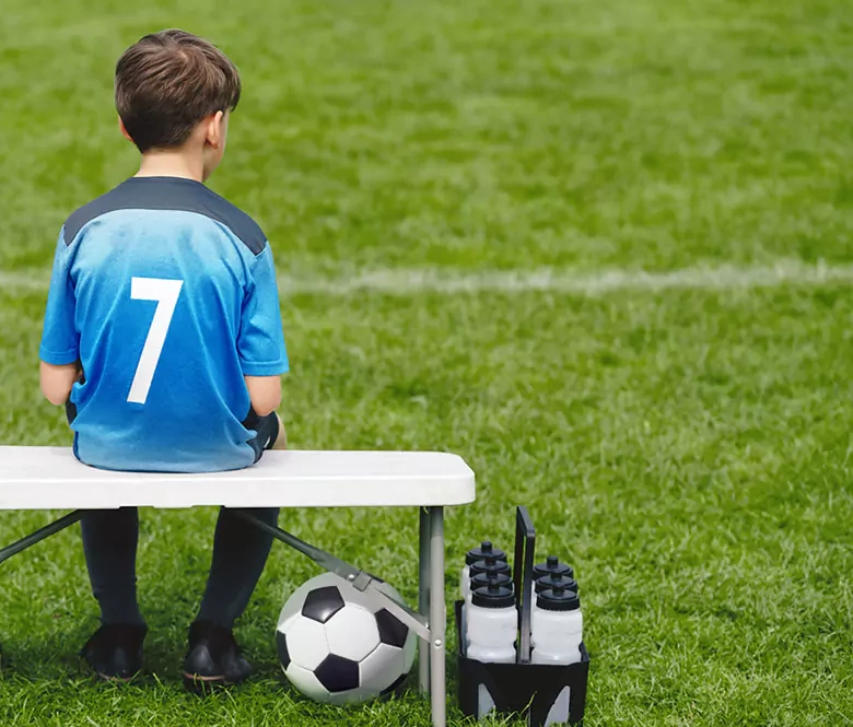 Ung gutt sitter alene på innbytterbenken på en fotballbane. Illustrasjonsbilde til kundecase om Zuccarellostiftelsen