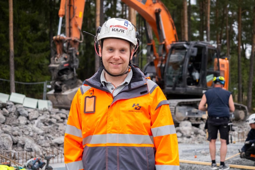 En bygningsarbeider i synlig jakke og hjelm smiler til kameraet mens han snakker om SmartDok og Tripletex