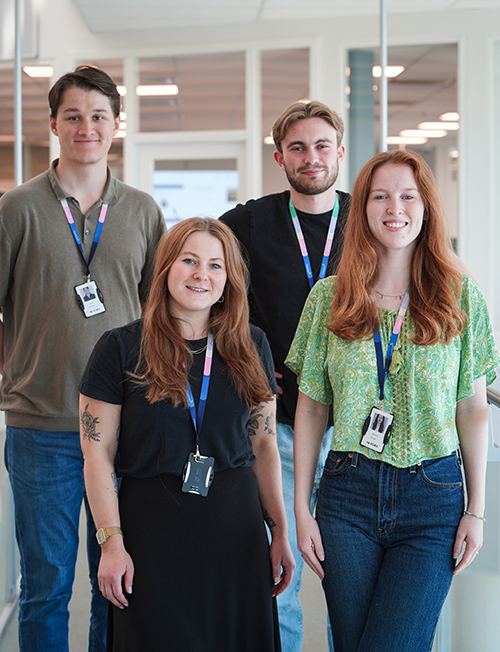Fire sommerstudenter i Tripletex, står innendørs,  smiler til kameraet.