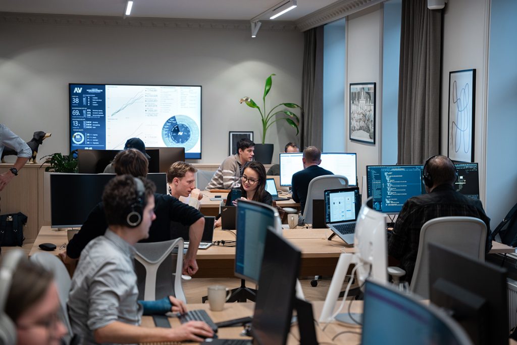 Folk som jobber i kontorlandskapet til Alv, med en digital dashbordskjerm på veggen.