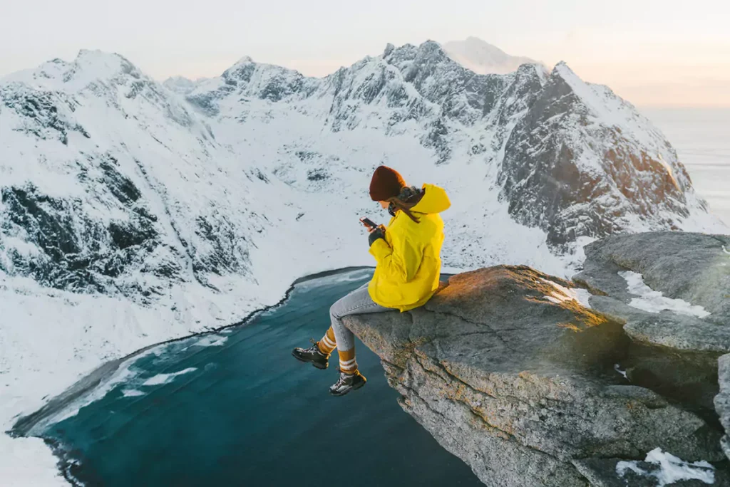 Kvinnelig influencer som sitter på en fjellknaus med snødekte fjell foran seg. Til sak artikkel om skatteregler.