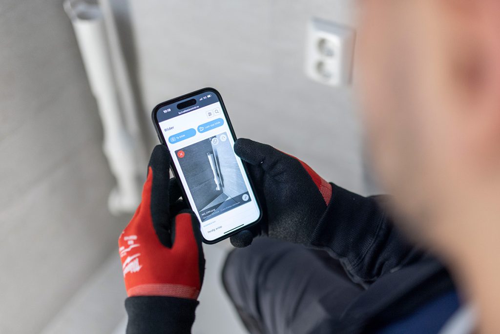 Person som har på seg svarte og røde hansker holder en smarttelefon som viser en app med et bilde.