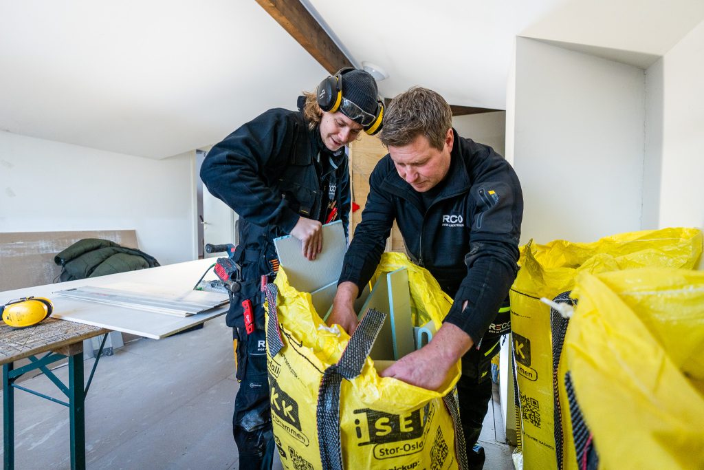 To bygningsarbeidere i verneutstyr ute på prosjekt håndterer avfall og legger materialer i gule poser.