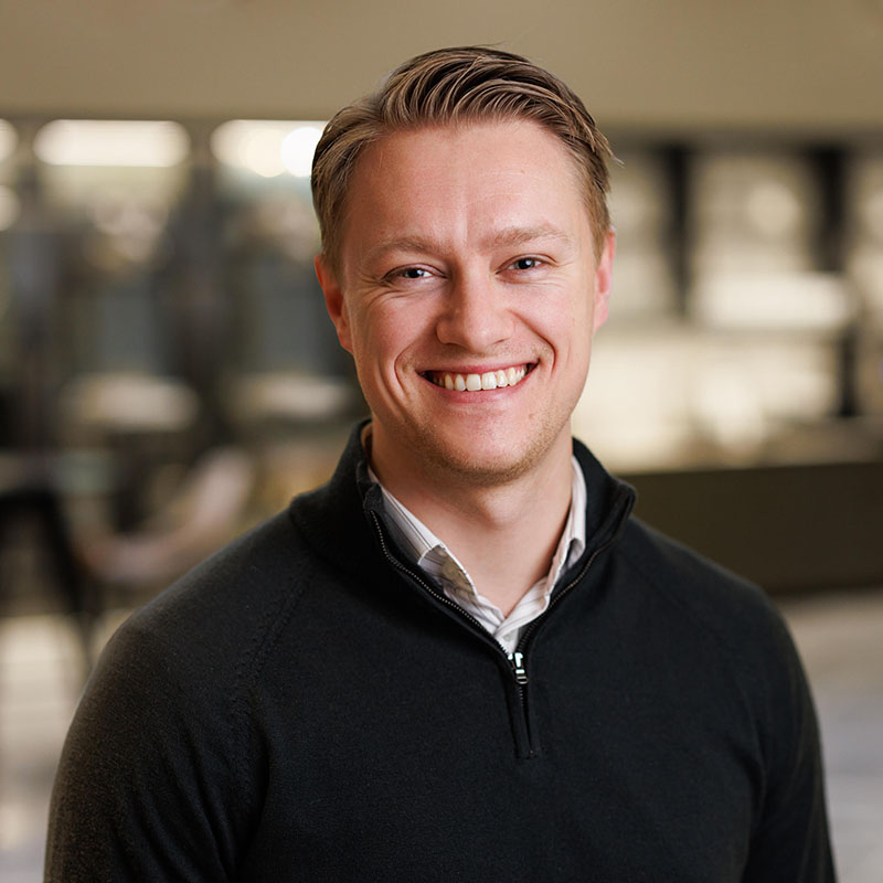 Håkon Bekkeseth, leder for onboarding i Tripletex, smiler til kameraet i en innendørs setting med uskarp bakgrunn.