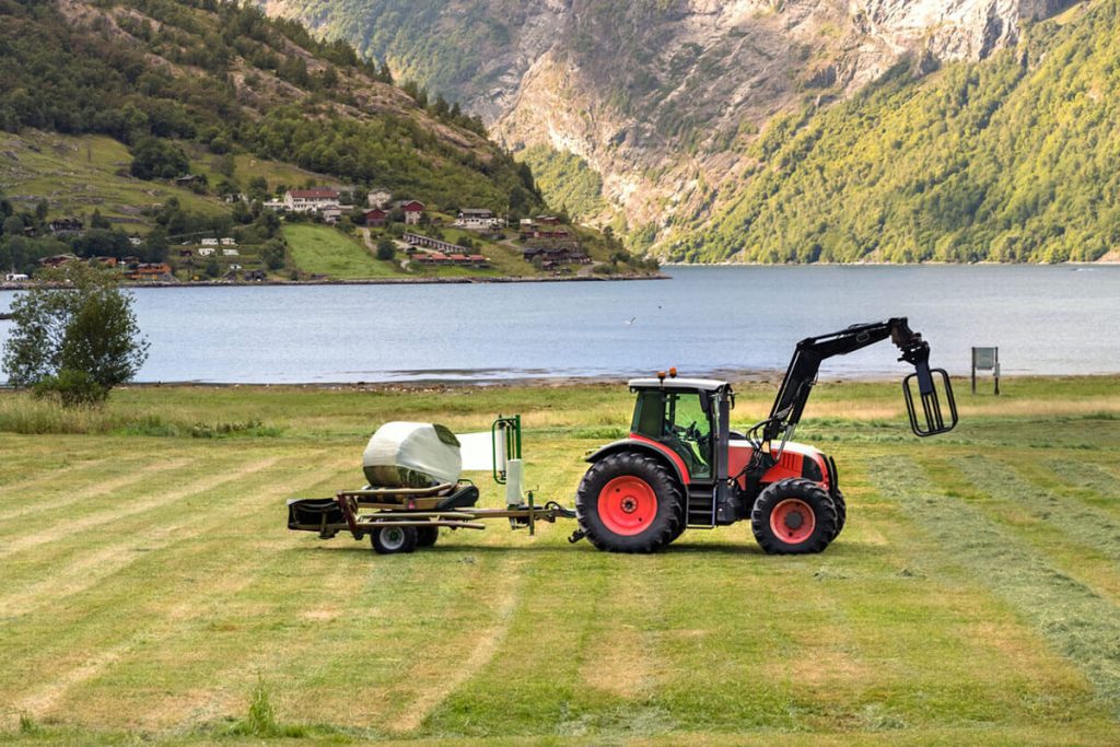 Traktor med frontlaster i en naturskjønn grønn mark nær en innsjø og fjell, til artikkel om regnskapsprogram for landbruk