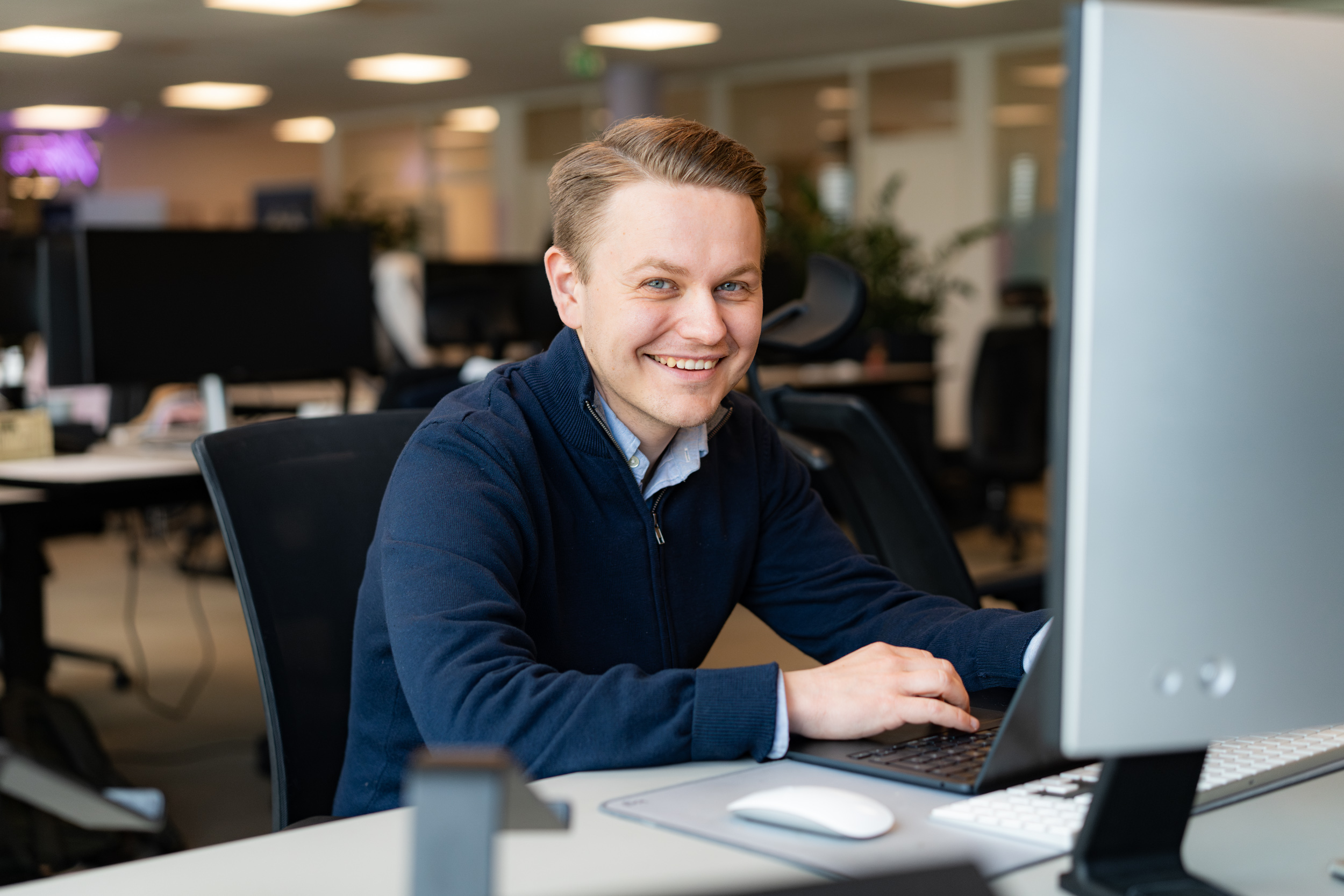 En smilende mann som sitter ved et skrivebord på et kontor og jobber på en datamaskin med hendene på tastaturet, konsentrert om å forberede årsoppgjøret.