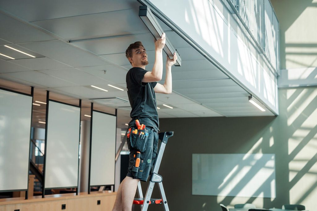 Elektriker som står på en stige og jobber, som illustrasjon til sak om prosjektoppfølging.