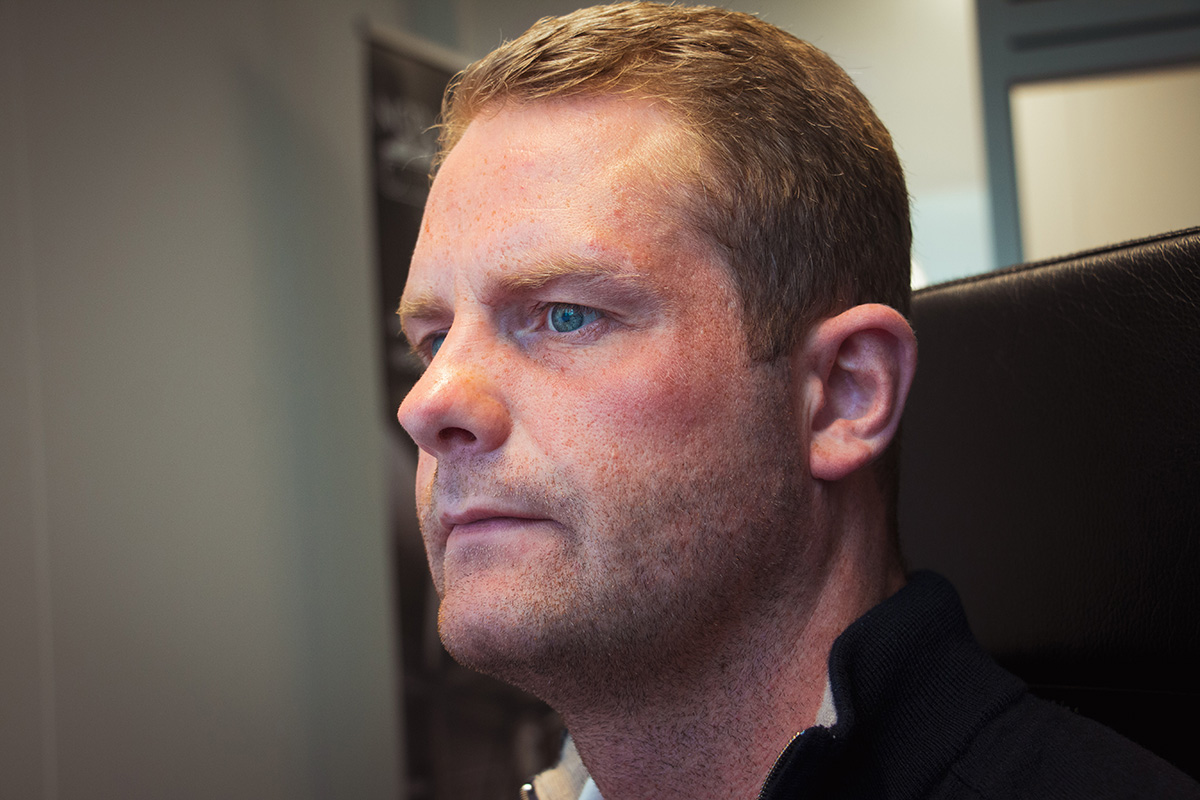 En mann med kort lysebrunt hår sitter i en kontorstol og ser intenst på en dataskjerm.