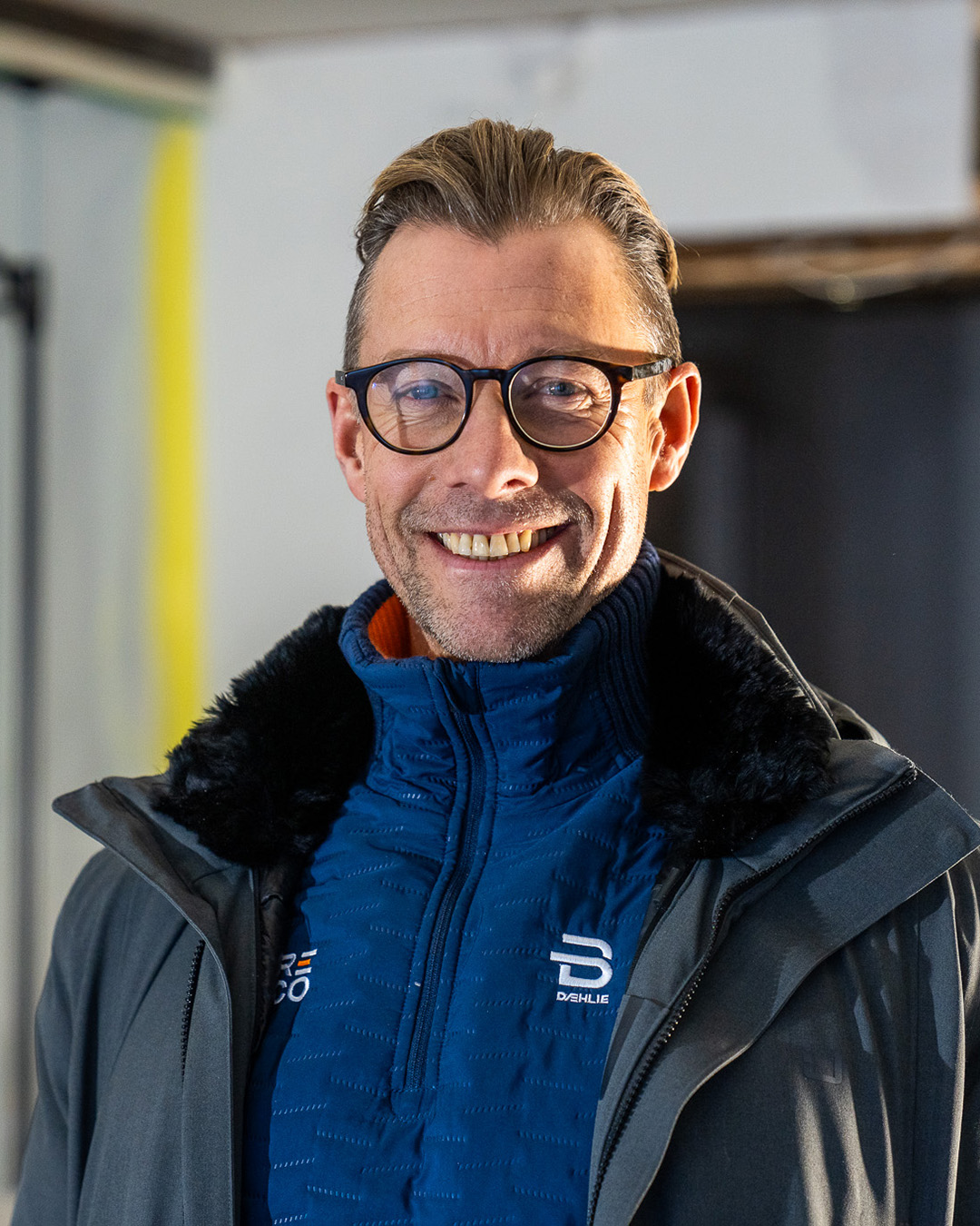 En person med solbriller og rød jakke holder opp en stor hvit solskjerm.