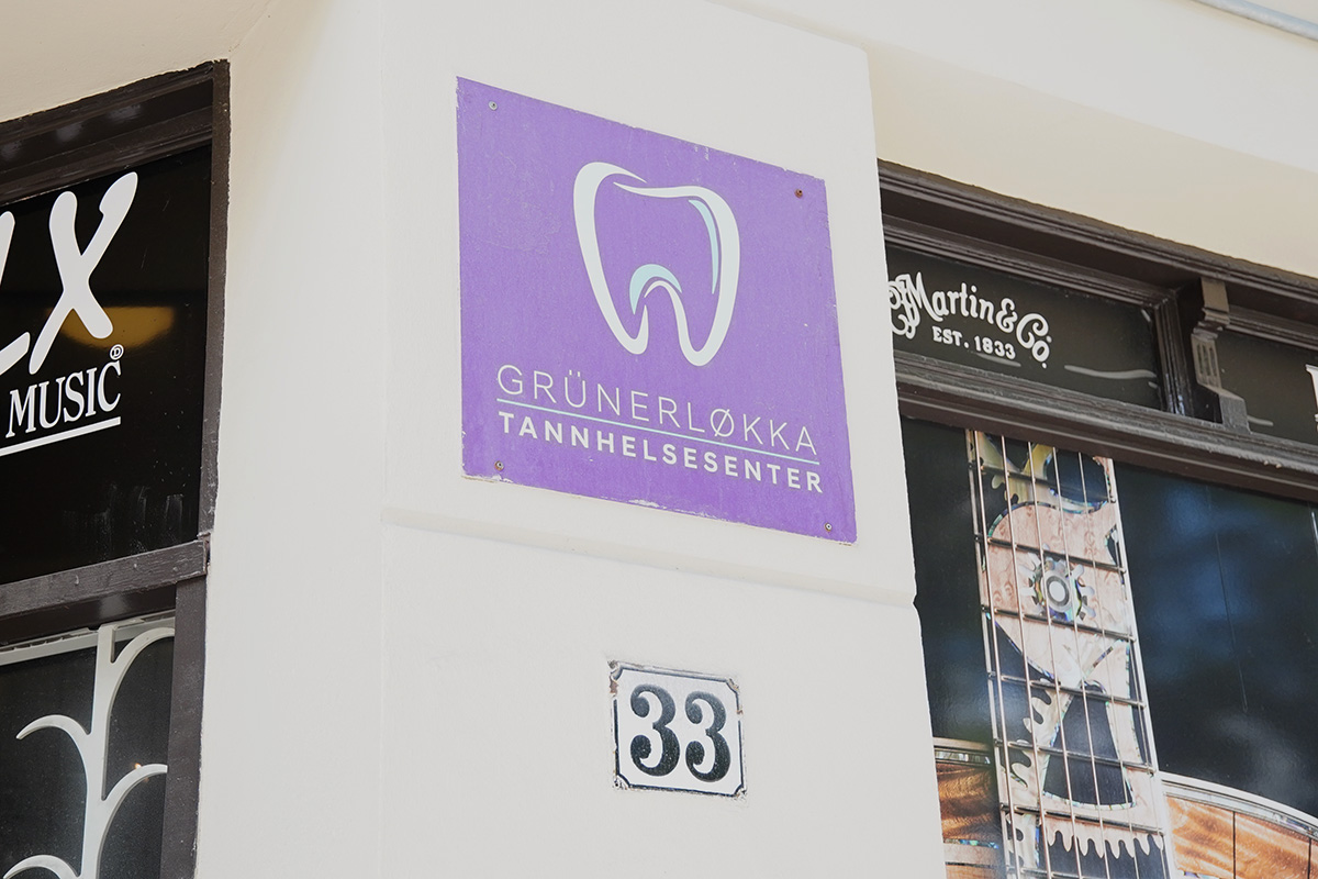 Et lilla skilt med tannlogo og teksten "Grünerløkka Tannhelsesenter" står over tallet 33 på en bygnings fasade.