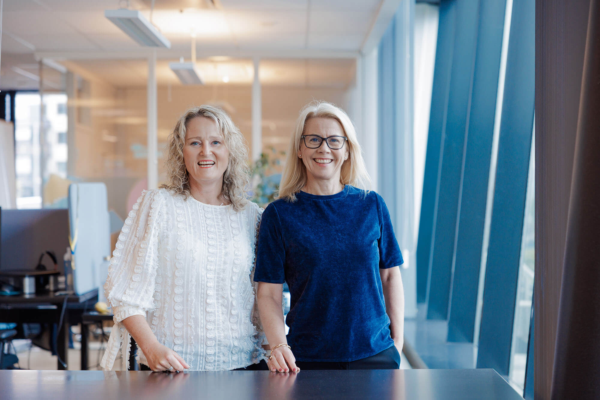 Hege Oustad og Lise Ekanger, TRipletex-gründere, står i kontorlandskap og smiler mot kamera.