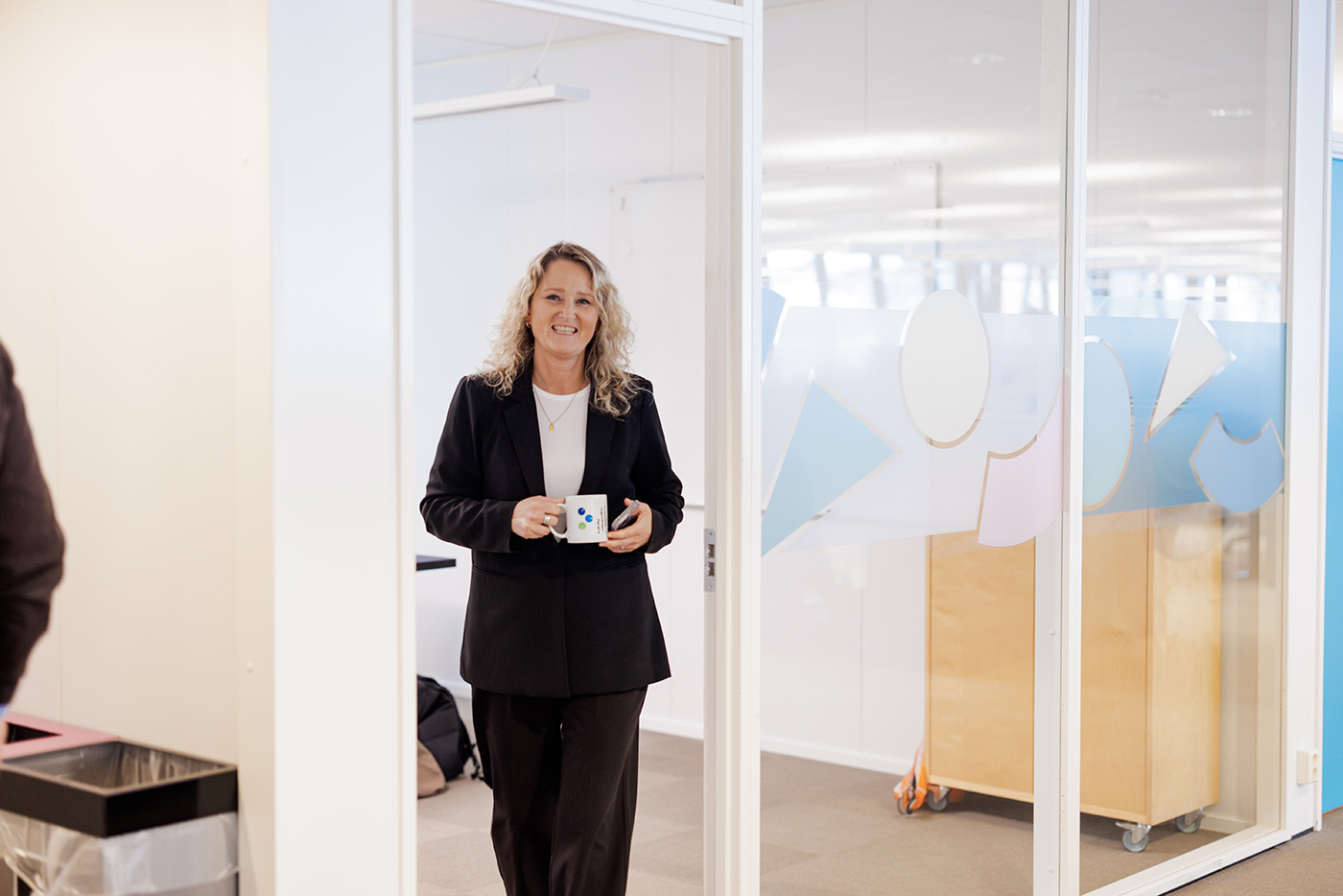 Lise Ekanger er direktør for strategiske kunderelasjoner i Tripletex. En kvinne med blondt hår og briller står smilende i et kontormiljø med pulter, skjermer og mennesker i bakgrunnen.