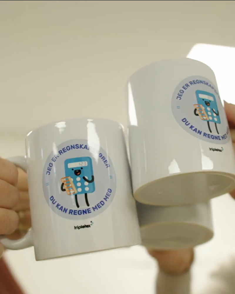 Tre hvite krus med identiske, runde logoer med en tegneseriekalkulator og norsk tekst holdes sammen i en skål.