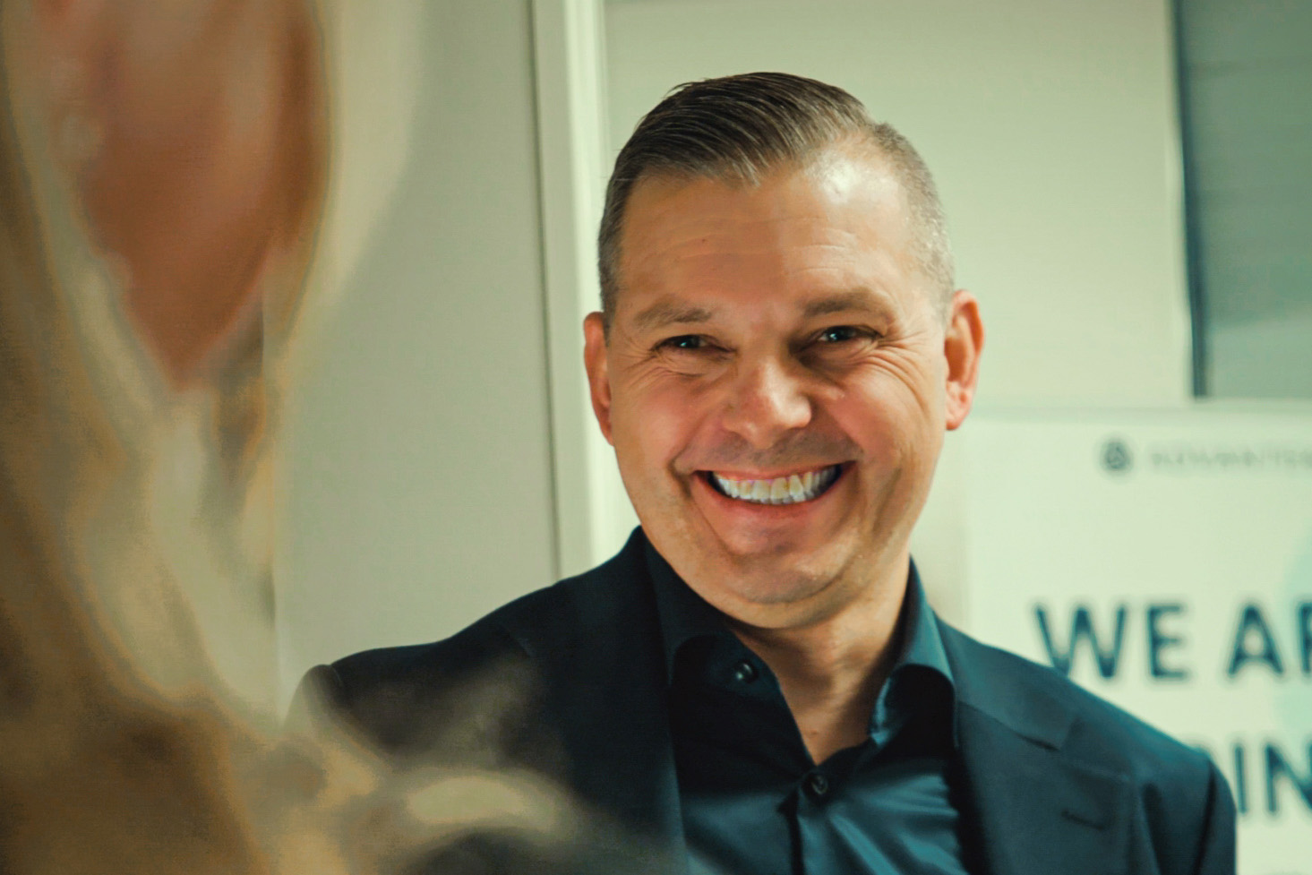 Lise Ekanger er direktør for strategiske kunderelasjoner i Tripletex. En kvinne med blondt hår og briller står smilende i et kontormiljø med pulter, skjermer og mennesker i bakgrunnen.