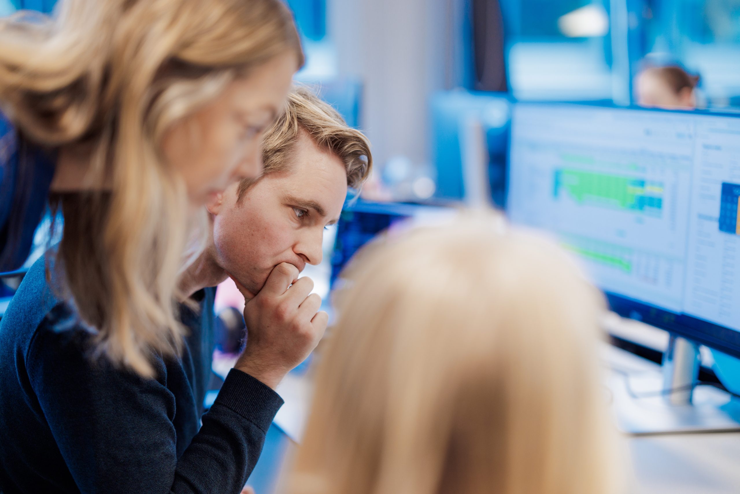 Tre personer ser nøye på en dataskjerm som viser data i et kontormiljø.