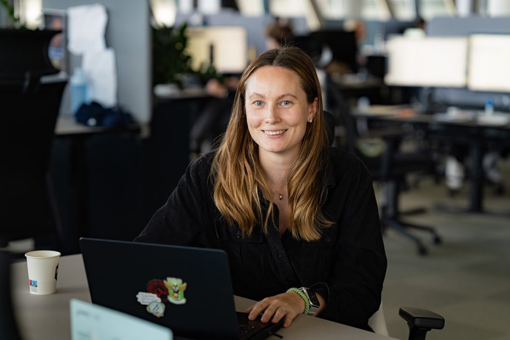 Kvinne sitter i et kontorlandskap, ser i kamera.