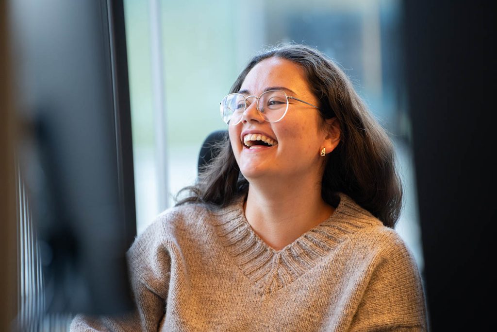 Portrettbilde av UX-designer Thale Meisfjord. Hun smiler mens hun kikker på en skjerm.
