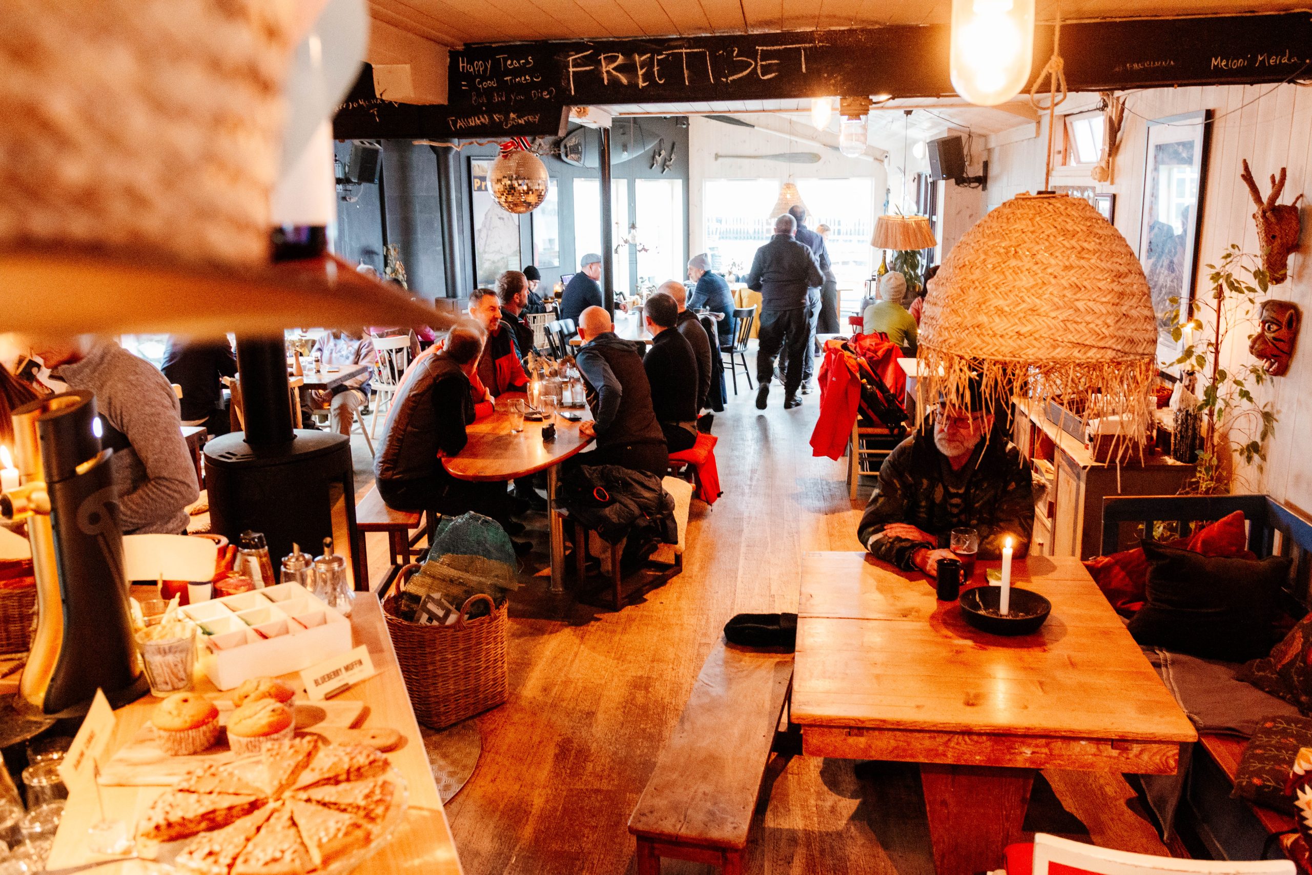 To menn står og snakker på et lite kafékjøkken; den ene holder et krus, mens den andre står ved disken med diverse kjøkkenutstyr.