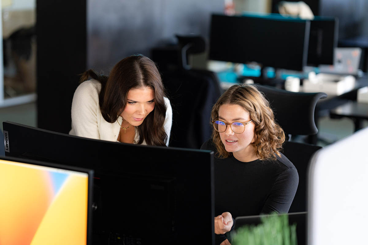 To personer sitter og ser på dataskjermer på et kontor.