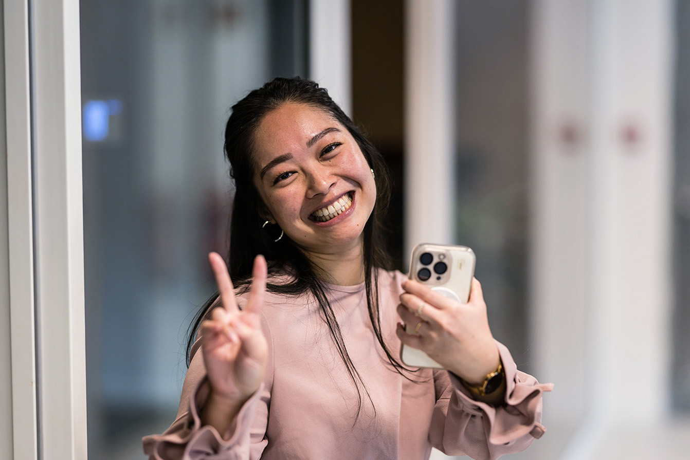 En smilende kvinne holder en smarttelefon for å ta en selfie. Kieu Mai er regnskapsfører i Solregn.